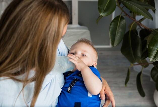 Un niño come un biberón de leche en brazos de su madre.