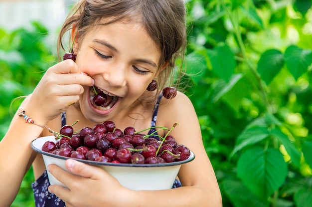 Niño come cerezas en el fondo del jardín