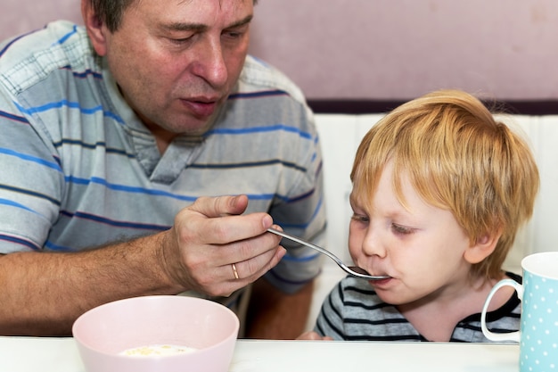 El niño come de la cuchara que sostiene el abuelo