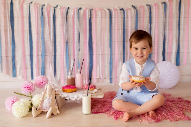 Un niño come donas y bebe leche de una pajita. buena comida para niños.