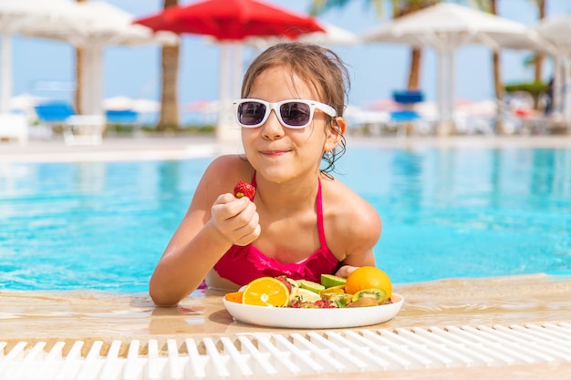 El niño come fruta cerca de la piscina. Niño.