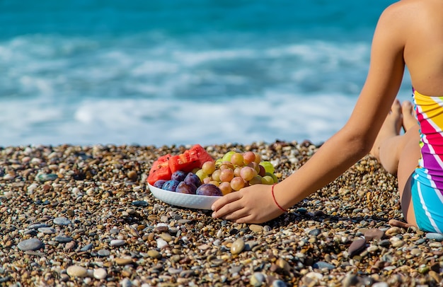 El niño come fruta junto al mar. Enfoque selectivo.