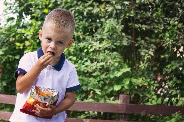 un niño come papas fritas de un paquete en el fondo de la naturaleza