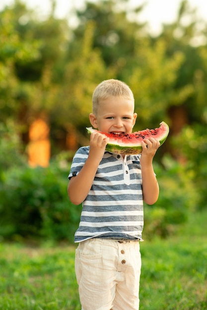 Foto niño come sandía al aire libre. vacaciones de verano en el campo.