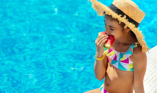 El niño come una sandía cerca de la piscina. Enfoque selectivo.