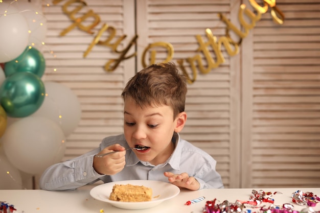 Un niño come un trozo de tarta de cumpleaños con una vela Bolas con una guirnalda en el fondo