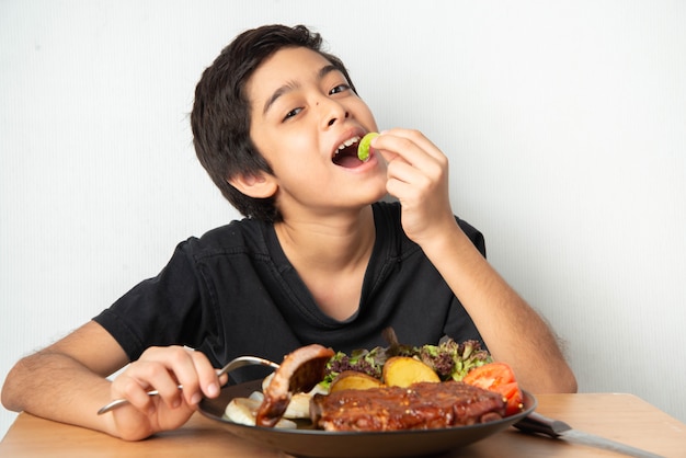 Niño comiendo costillas parrilla de cerdo con cara feliz