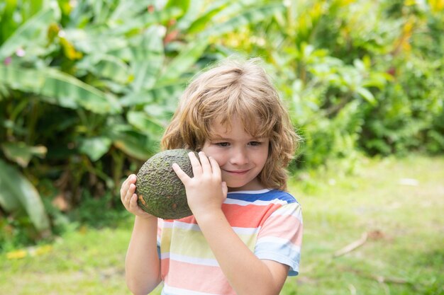 Niño comiendo y disfrutando de un aguacate sobre un fondo de naturaleza. Concepto de comida sana para niños.