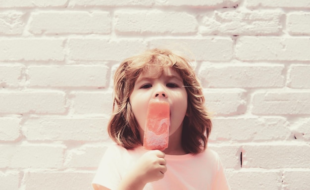 Niño comiendo helado en un fondo de pared rosa