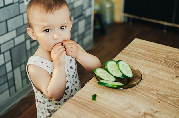 Niño comiendo un pepino fresco en rodajas en la cocina