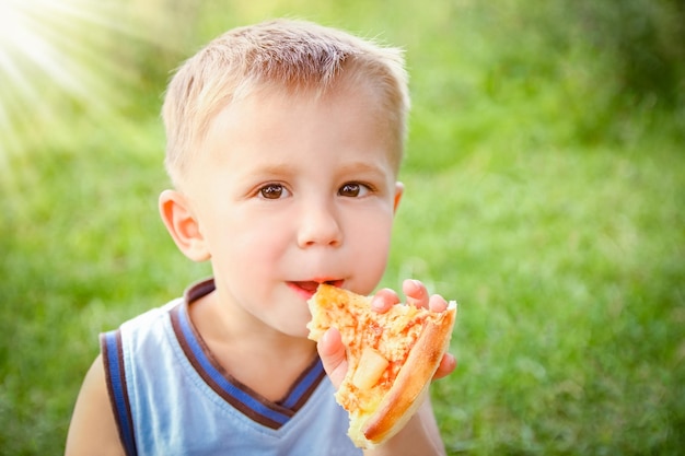 Niño comiendo una pizza sabrosa sobre la naturaleza de la hierba en el parque