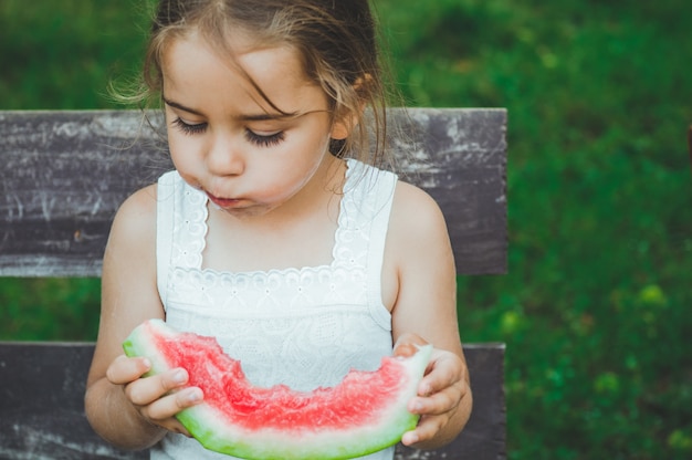 Niño comiendo sandía en el jardín. Los niños comen frutas al aire libre. Merienda saludable para niños. Niña jugando en el jardín mordiendo una rodaja de sandía.