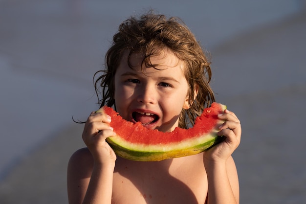 Niño comiendo sandía en la playa niño sosteniendo una rodaja de sandía en la playa vacaciones de verano divertidas y