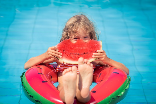 Niño comiendo sandía en una sandía inflable en la piscina.