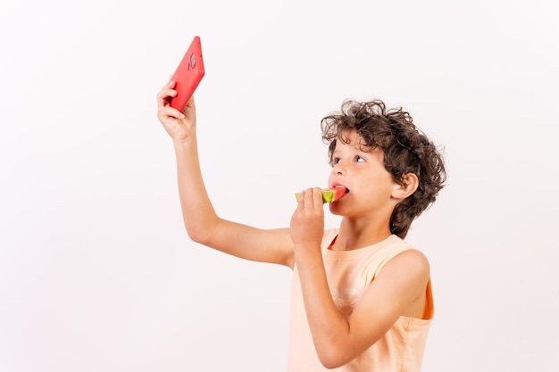 Niño comiendo una sandía y tomando un selfie vacaciones de verano Fondo blanco con copiar y pegar