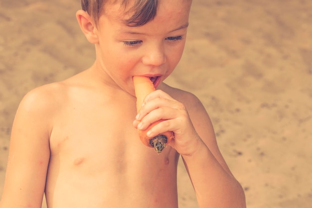 Niño comiendo zanahoria en la playa de arena