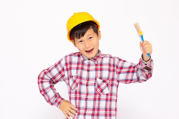 Niño como trabajador de la construcción con casco amarillo con un pincel en la mano