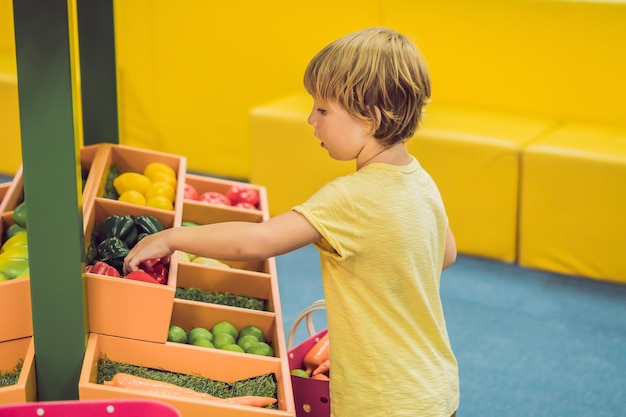 Un niño compra verduras de juguete en un supermercado de juguetes.