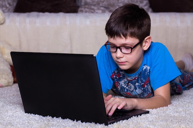 Un niño con una computadora portátil tirada en el suelo en casa sobre la alfombra Tecnología Internet concepto de comunicación moderna