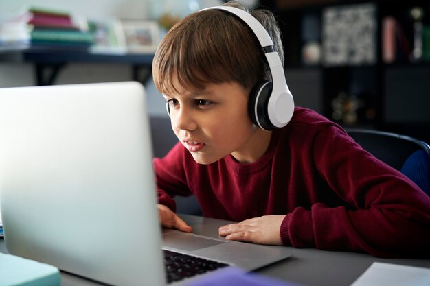 Niño concentrado con auriculares frente a la computadora portátil