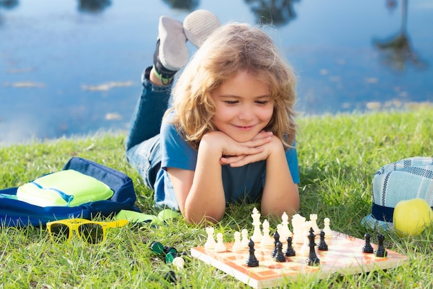 Niño concentrado desarrollando estrategia de ajedrez jugando juego de mesa en el patio trasero tendido en el césped