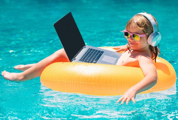 Niño de concepto de trabajo independiente que trabaja en una computadora portátil en la piscina junto a la piscina tecnología en línea de verano