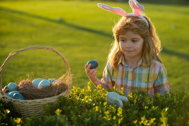 Niño conejito con orejas de conejo. Niño cazando huevos de pascua en el patio trasero.