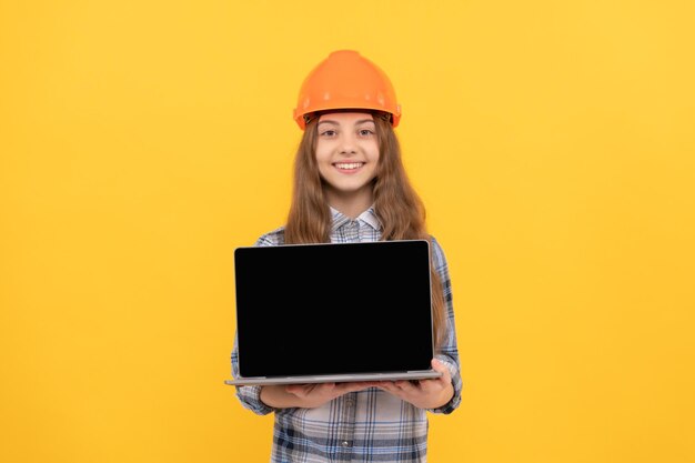 Niño constructor mantenga la computadora. construcción y edificación. presentación. niño trabajador feliz usa casco. educación infantil en línea. feliz Día del Trabajo. copie el espacio. jovencita en casco presentando portátil.