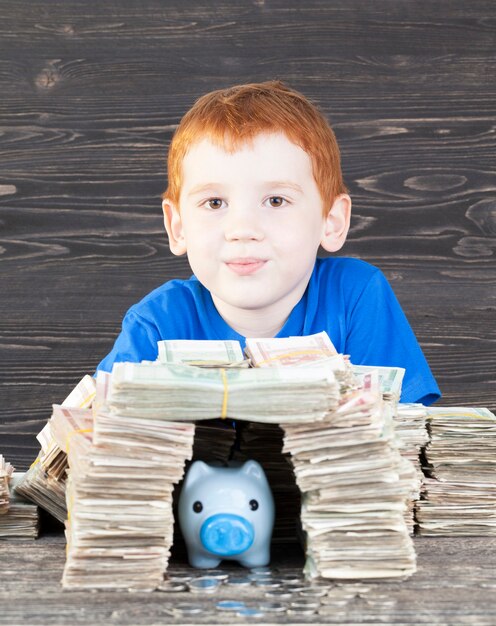 Niño construido para su hucha de cerdo azul con monedas casa de paquetes de papel moneda, primer plano