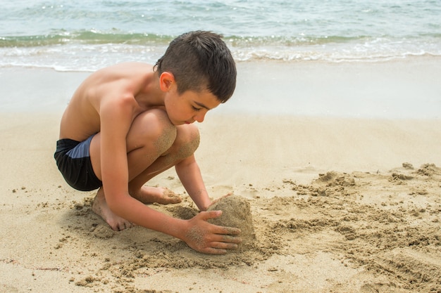 Niño construye un castillo de arena en la playa junto al mar