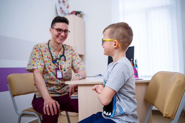 Un niño en el consultorio del médico, el médico escucha los pulmones del niño. Examen médico del niño