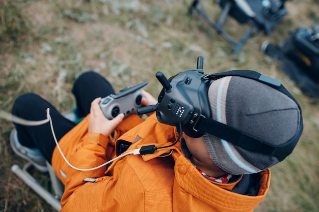 Niño controlando drone fpv quadcopter para fotografía aérea y videografía con control remoto de antena de gafas.