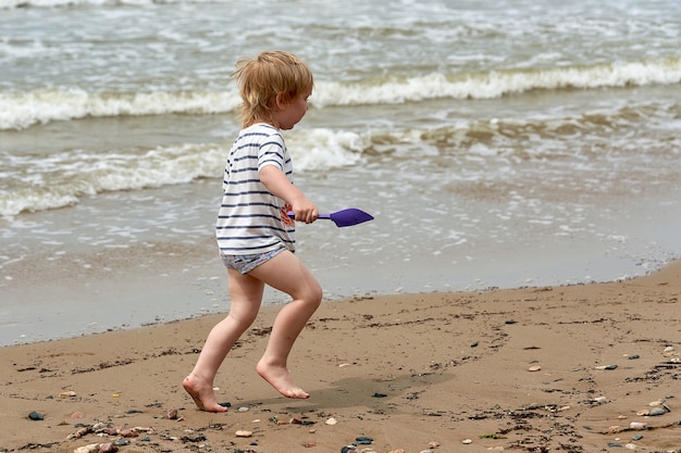 Un niño corre a lo largo de la playa de arena a lo largo de la orilla del mar.