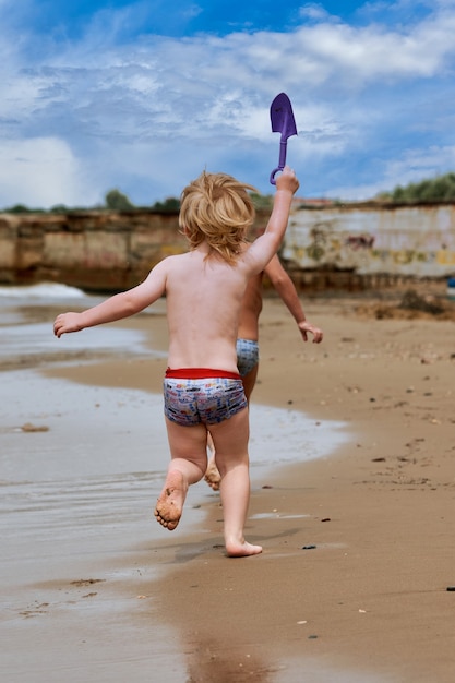 Foto un niño corre por la playa de arena junto a la orilla del mar. niño descansando sobre el mar