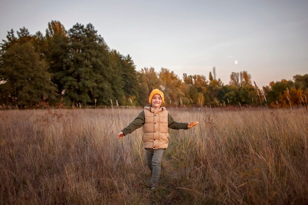 Niño corre solo camino a través de un prado seco sobre fondo hermoso bosque otoñal