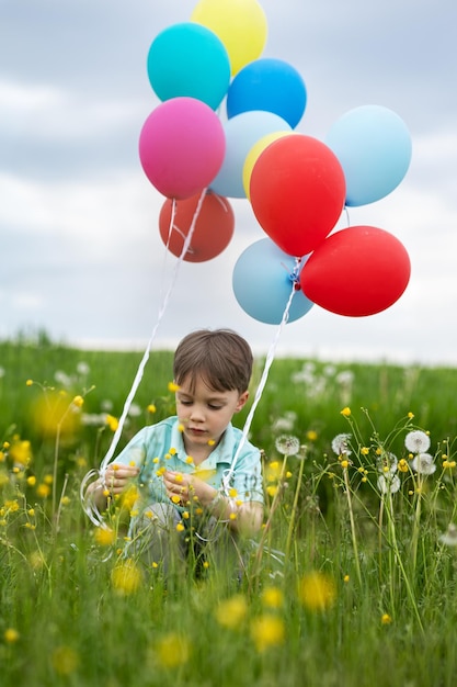 Niño de cuatro años con globos camina en un prado verde con dientes de león