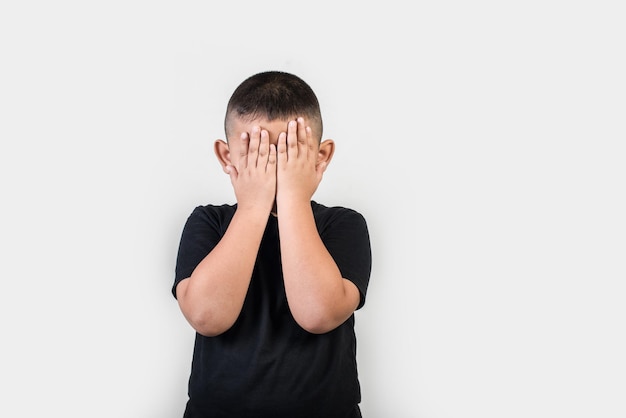 Foto niño cubriendo la cara mientras está de pie contra un fondo gris