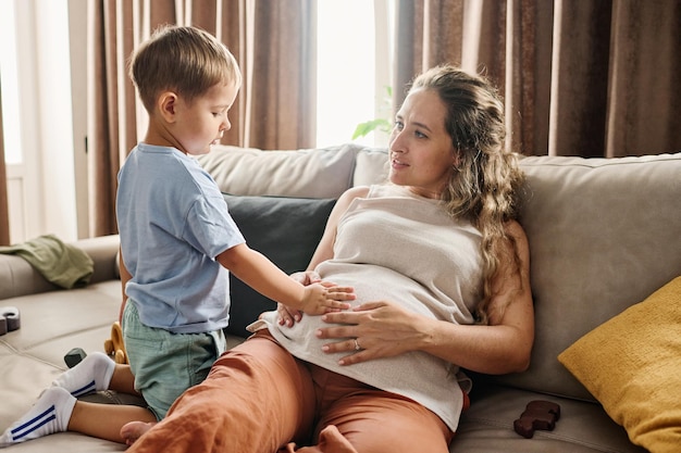 Niño curioso manteniendo la mano en el vientre de su madre embarazada