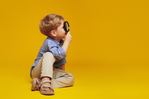 Foto niño curioso sentado en el suelo y mirando a través de una lupa en el espacio vacío libre para el texto