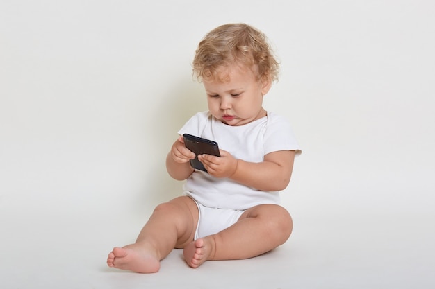 Niño curioso sentado en el suelo con el teléfono en las manos