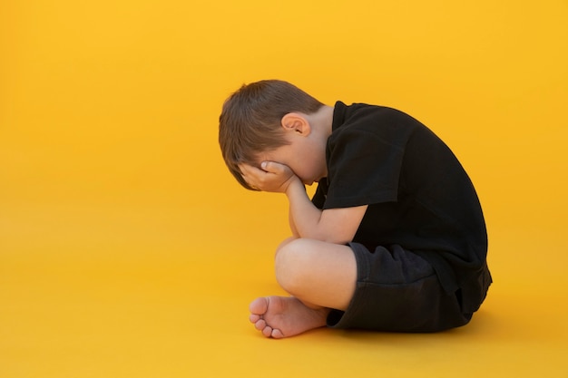 Niño cuya depresión está sentada en el suelo de color