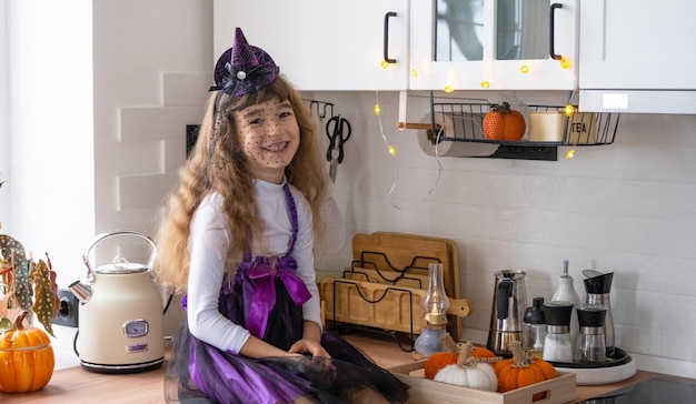 El niño decora la cocina en casa para Halloween La niña con un disfraz de bruja juega con la decoración para las fiestas Los murciélagos Jack Lantern Calabazas Comodidad otoñal en casa Loft de cocina Scandistyle