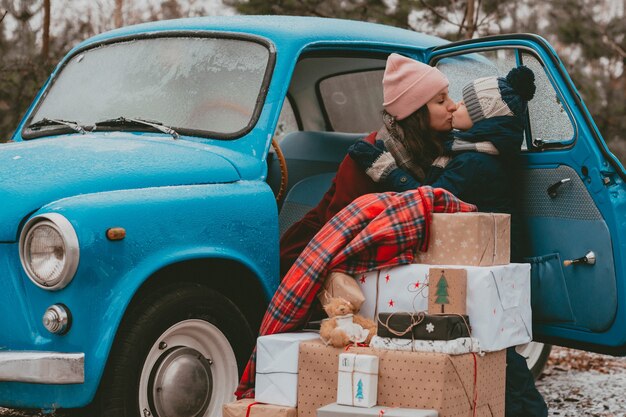 Niño decorado con un coche retro azul con cajas de regalo de ramas de árbol de navidad festivas en envoltura artesanal ...