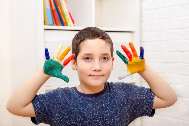 Foto un niño con dedos coloreados pintados muestra sus manos sentadas