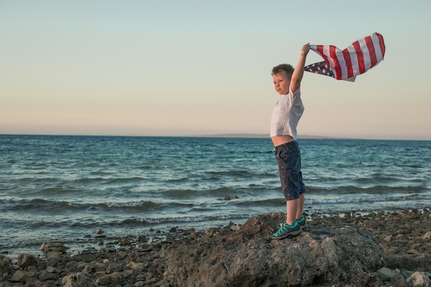 Niño deja volar la bandera americana en sus manos en el viento en el mar