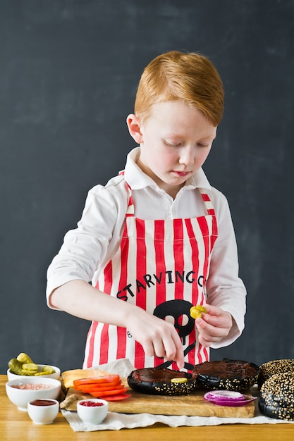 Un niño en un delantal de cocina en la hamburguesa de la cocina.