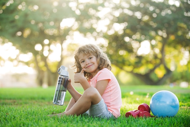 Niño deportivo bebiendo agua Concepto deportivo para niños Ejercicios de salud y energía para niños con mancuernas Estilo de vida saludable para niños