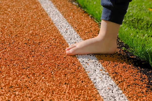 Niño descalzo en pista de atletismo naranja. Principiantes al atletismo. Pequeño atleta. Futuro campeón.