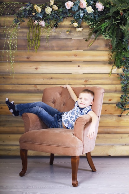 Un niño descansa sobre un sillón. Muchacho serio joven en ropa casual posando.