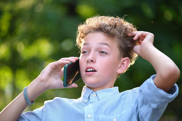 Niño desconcertado joven hablando por teléfono celular al aire libre en el parque de verano